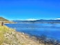 Een rustig meer met helderblauw water, omringd door glooiende heuvels en verre bergen onder een heldere lucht.