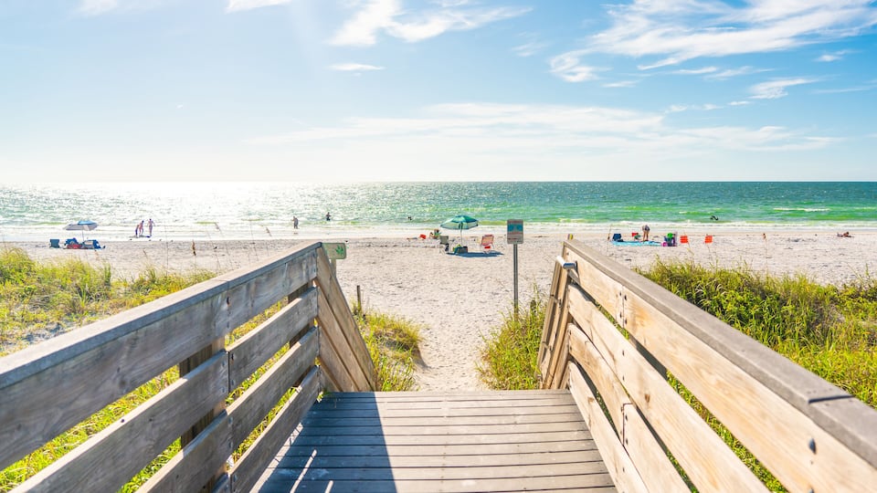 A wooden boardwalk leading to a beach with people and umbrellas.
