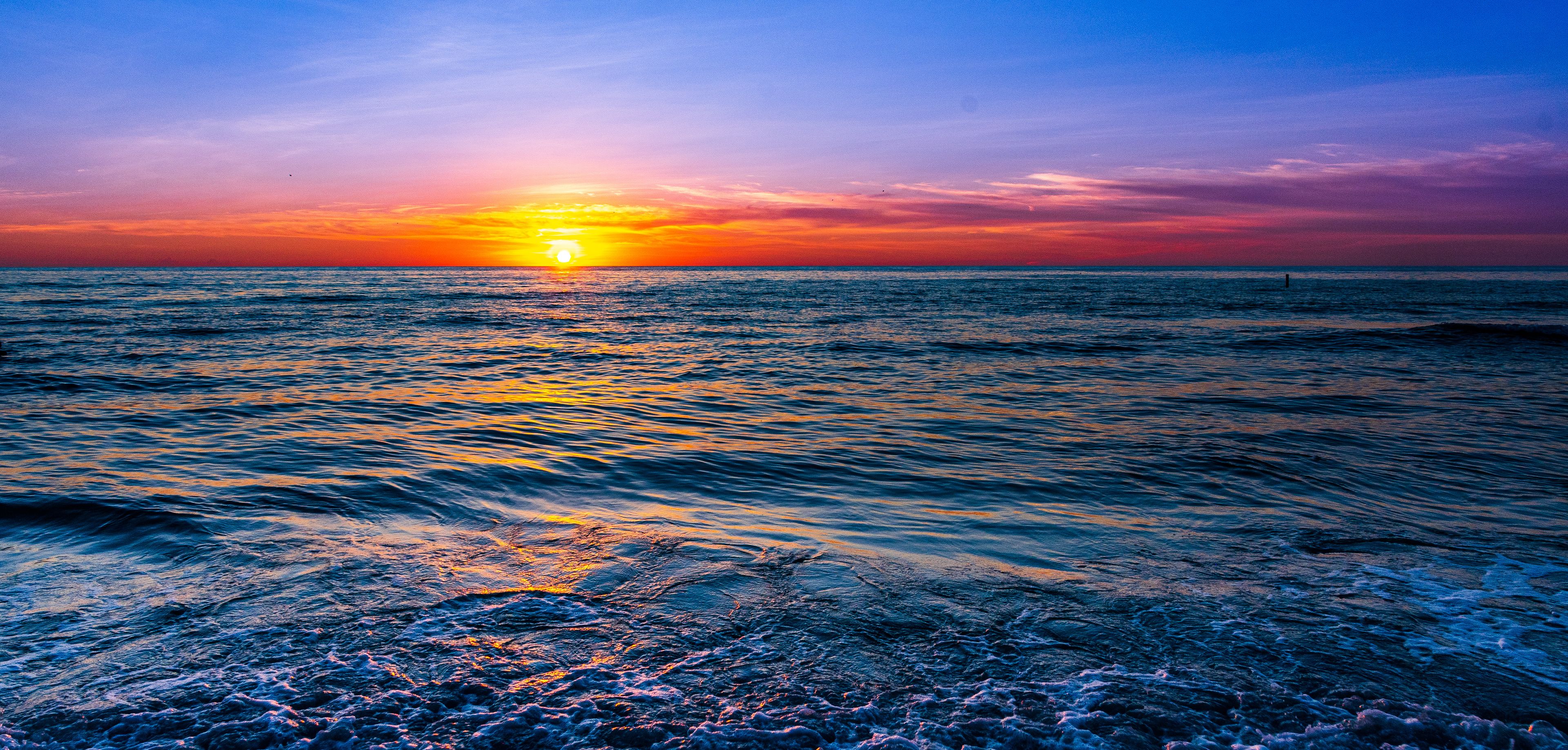 Un tramonto sull'oceano con le onde che riflettono i colori del cielo.