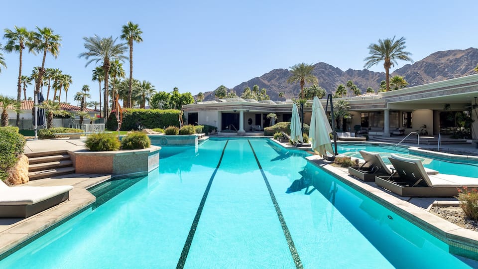A swimming pool with lounge chairs, palm trees, and mountains in the background.