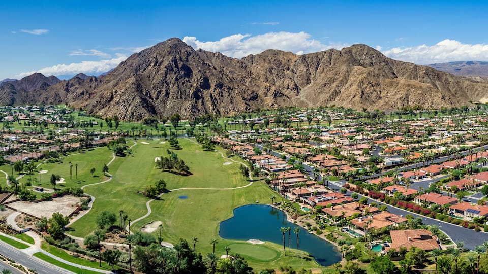 A residential area with a golf course, a lake, and mountains in the background.