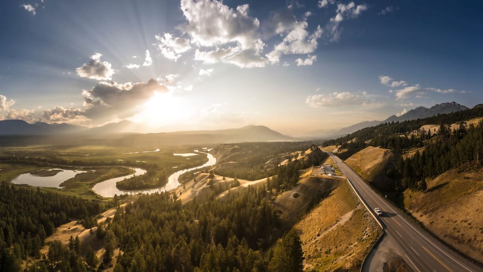A winding river through a mountainous landscape with a road on the right.