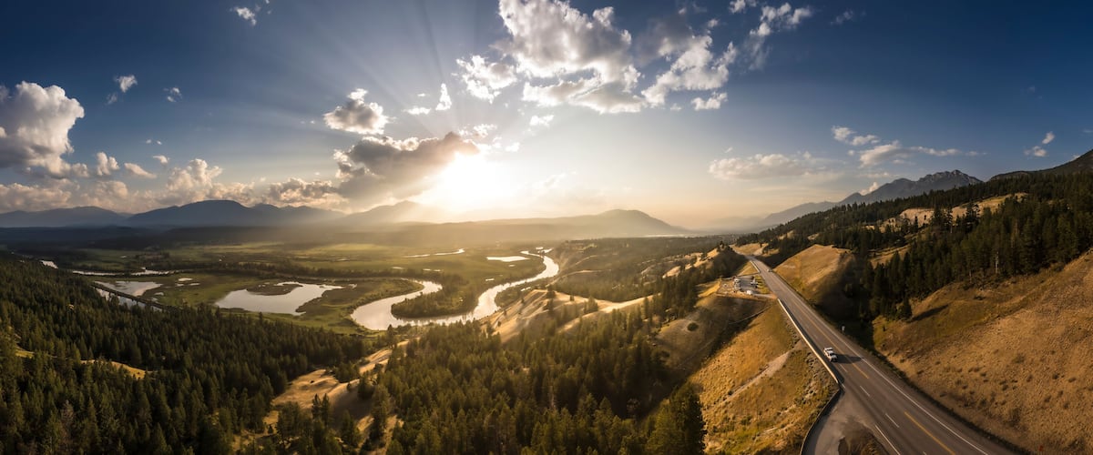 A winding river through a mountainous landscape with a road on the right.