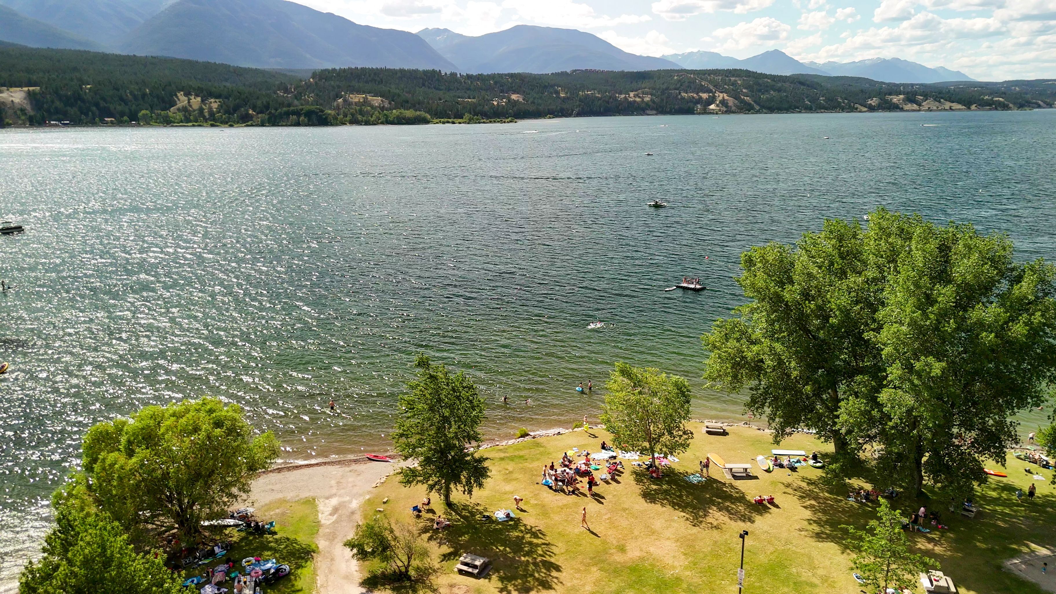 A lake with boats, a grassy area with people, and mountains in the background.