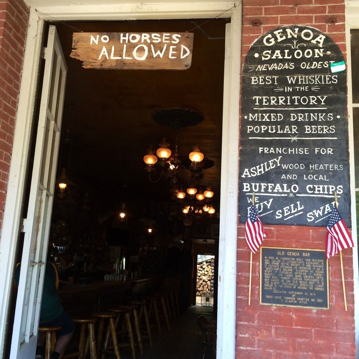 A bar with a 'No Horses Allowed' sign, vintage lighting, and a signboard advertising Genao Saloon as Nevada's oldest whisky bar.