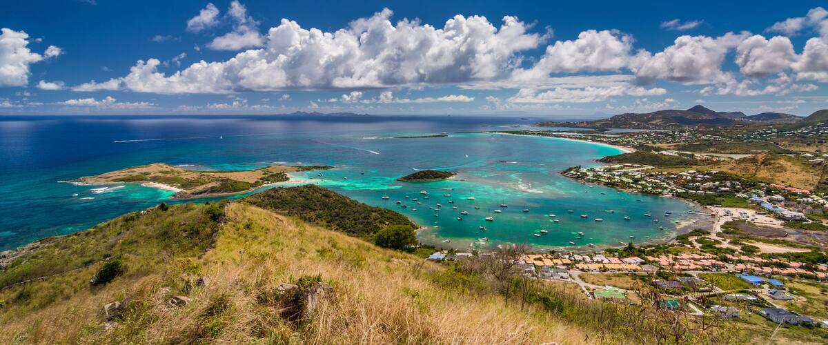 A coastal landscape with turquoise waters, boats, and a town with houses and buildings.
