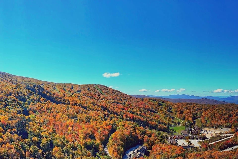 Un paysage montagneux aux couleurs automnales, une route sinueuse et un petit village avec des bâtiments et un espace de stationnement.