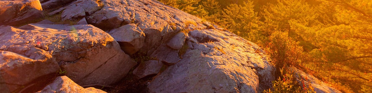 A sunset over a mountainous landscape with rocky outcrops and dense forest.