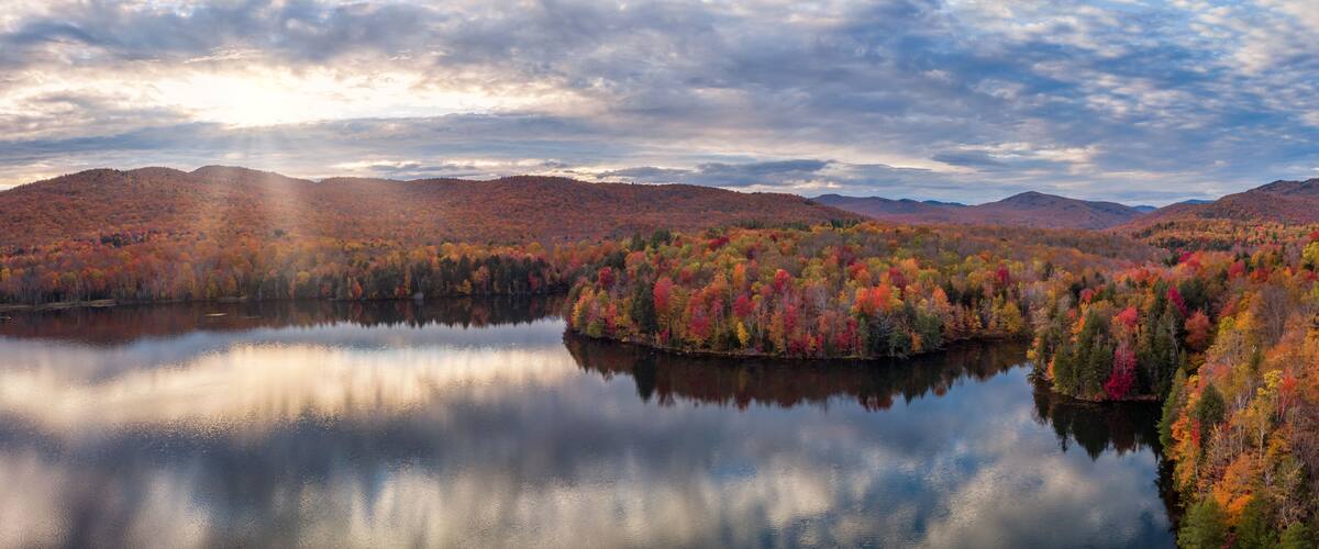 A calm lake surrounded by colorful autumn foliage and distant mountains.