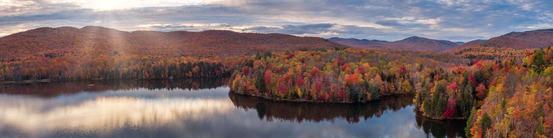 A calm lake surrounded by colorful autumn foliage and distant mountains.
