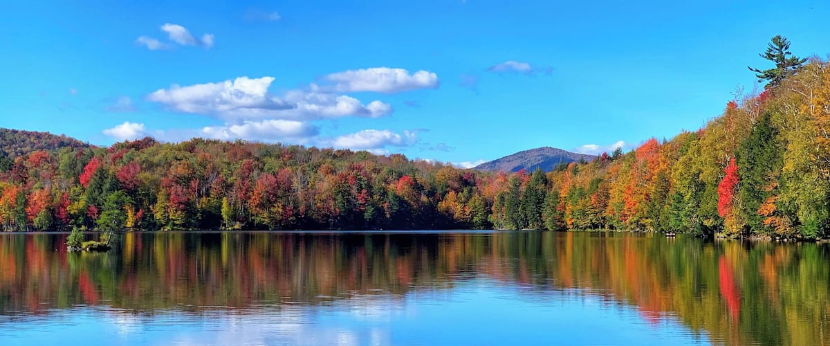A calm lake reflecting colorful autumn trees and a clear blue sky.