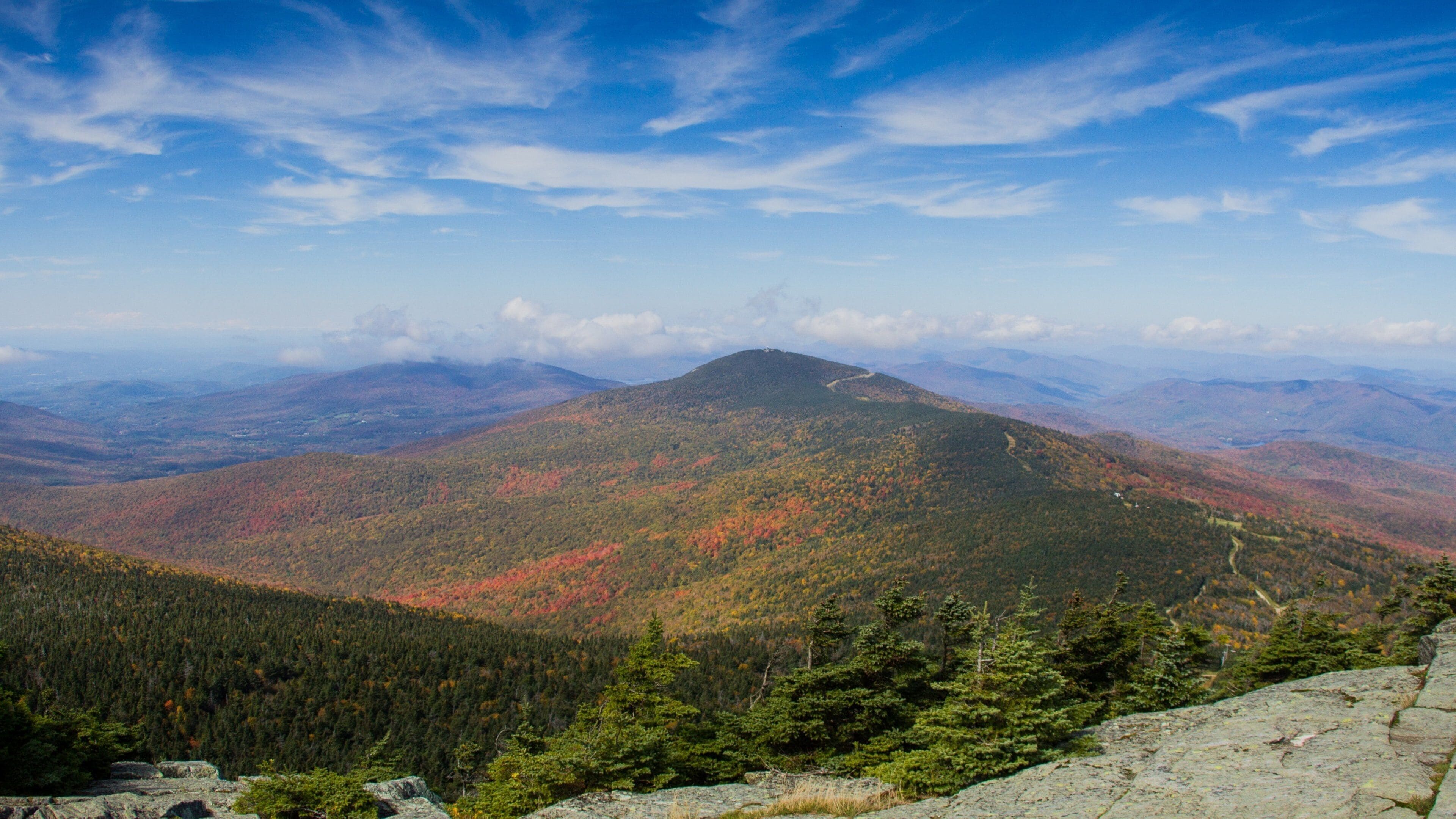 A mountain range with autumn foliage, a clear sky, and distant valleys.