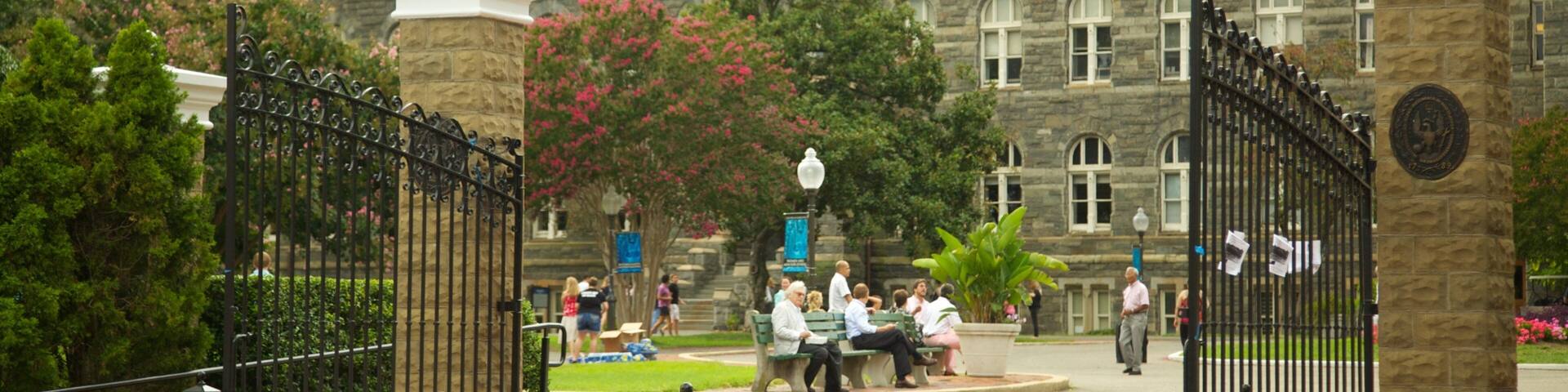 A historic building with ornate architecture, a gated entrance, and a well-maintained garden with benches.