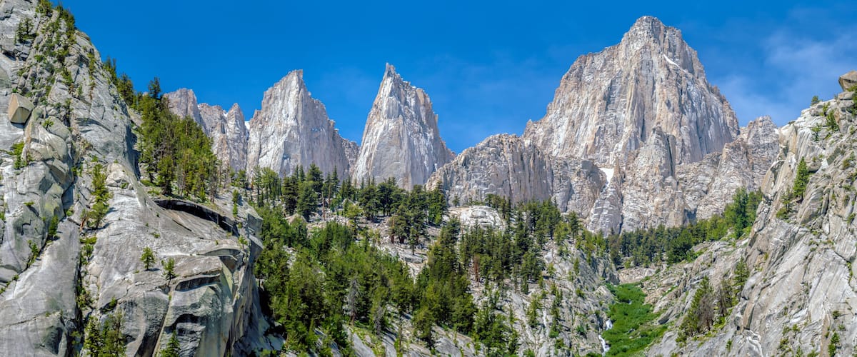 A rugged mountain landscape with prominent rocky peaks and dense forest.