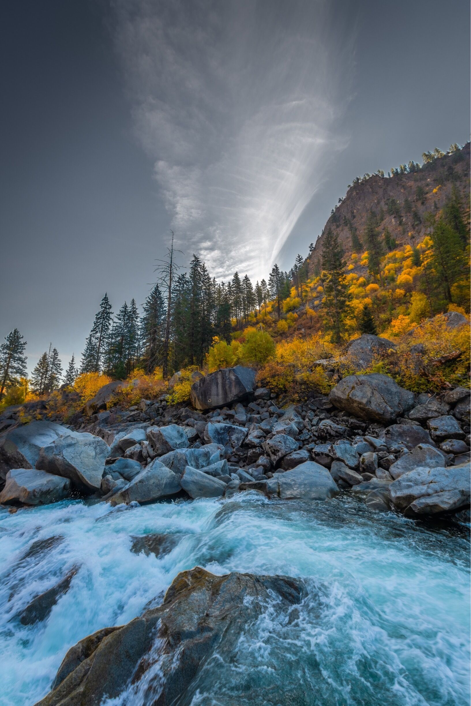 A cloudless fall morning on the Wenatchee River near Leavenworth, the sky broken by a spreading contrail at sunrise.