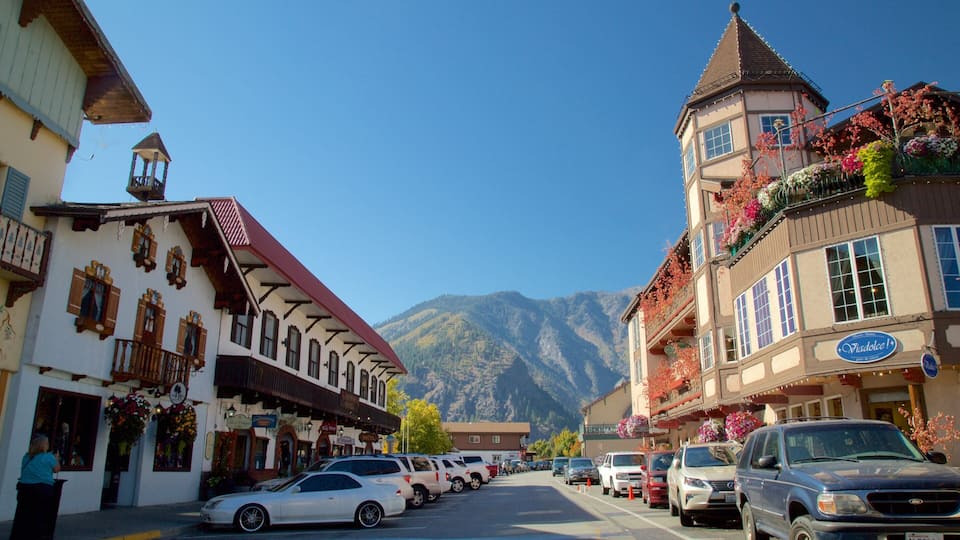 A mountain town street with traditional buildings, parked cars, and a mountain backdrop.