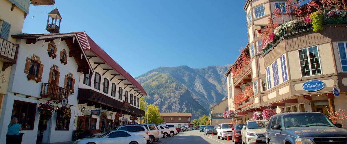 A mountain town street with traditional buildings, parked cars, and a mountain backdrop.