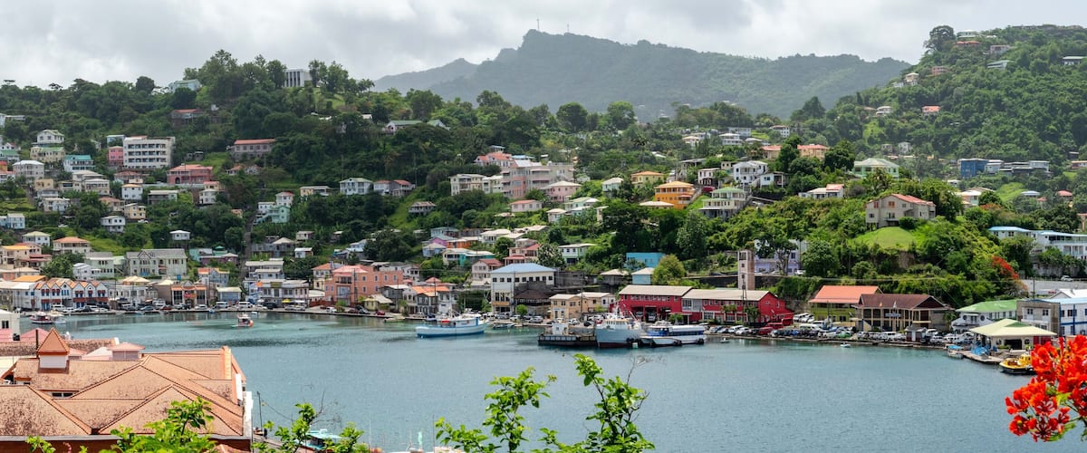 A coastal town with colorful buildings, a harbor with boats, and lush green hills in the background.