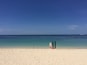 En strand med to surfbrædder, der hviler op ad en pæl, en klar blå himmel og et roligt hav med både i horisonten.