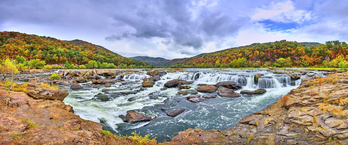Un río con múltiples cascadas rodeado de árboles de colores otoñales y terreno rocoso.