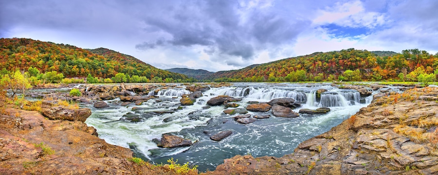 Ein Fluss mit mehreren Wasserfällen, umgeben von herbstlich gefärbten Bäumen und felsigem Gelände.