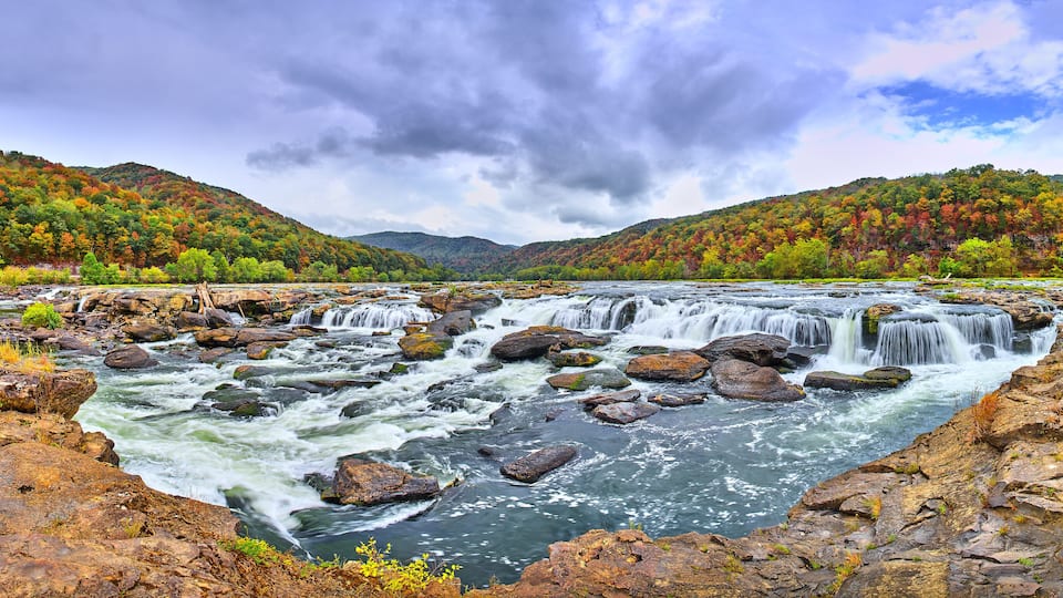 A river with multiple waterfalls surrounded by autumn-colored trees and rocky terrain.