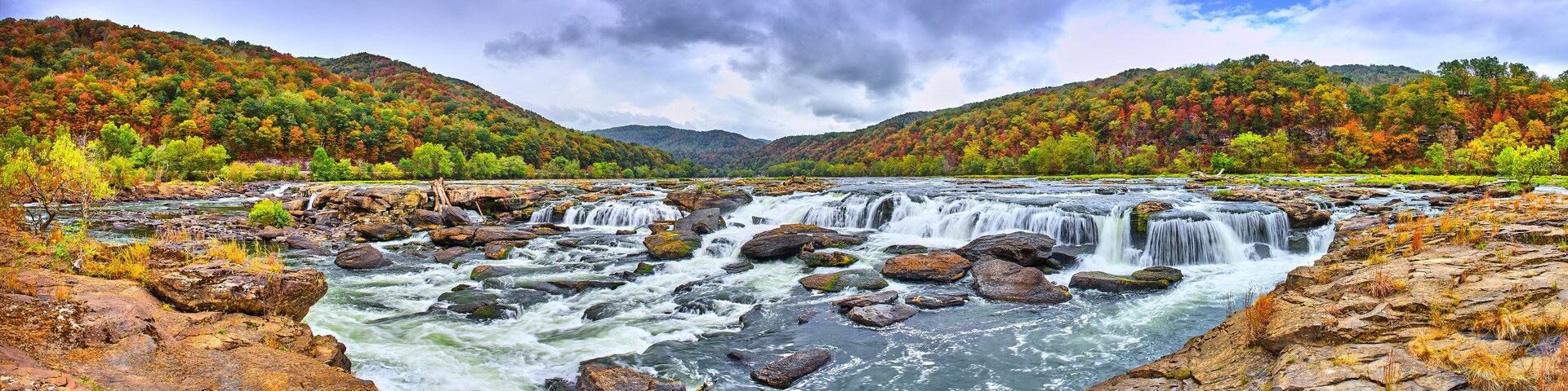 Un río con múltiples cascadas rodeado de árboles de colores otoñales y terreno rocoso.