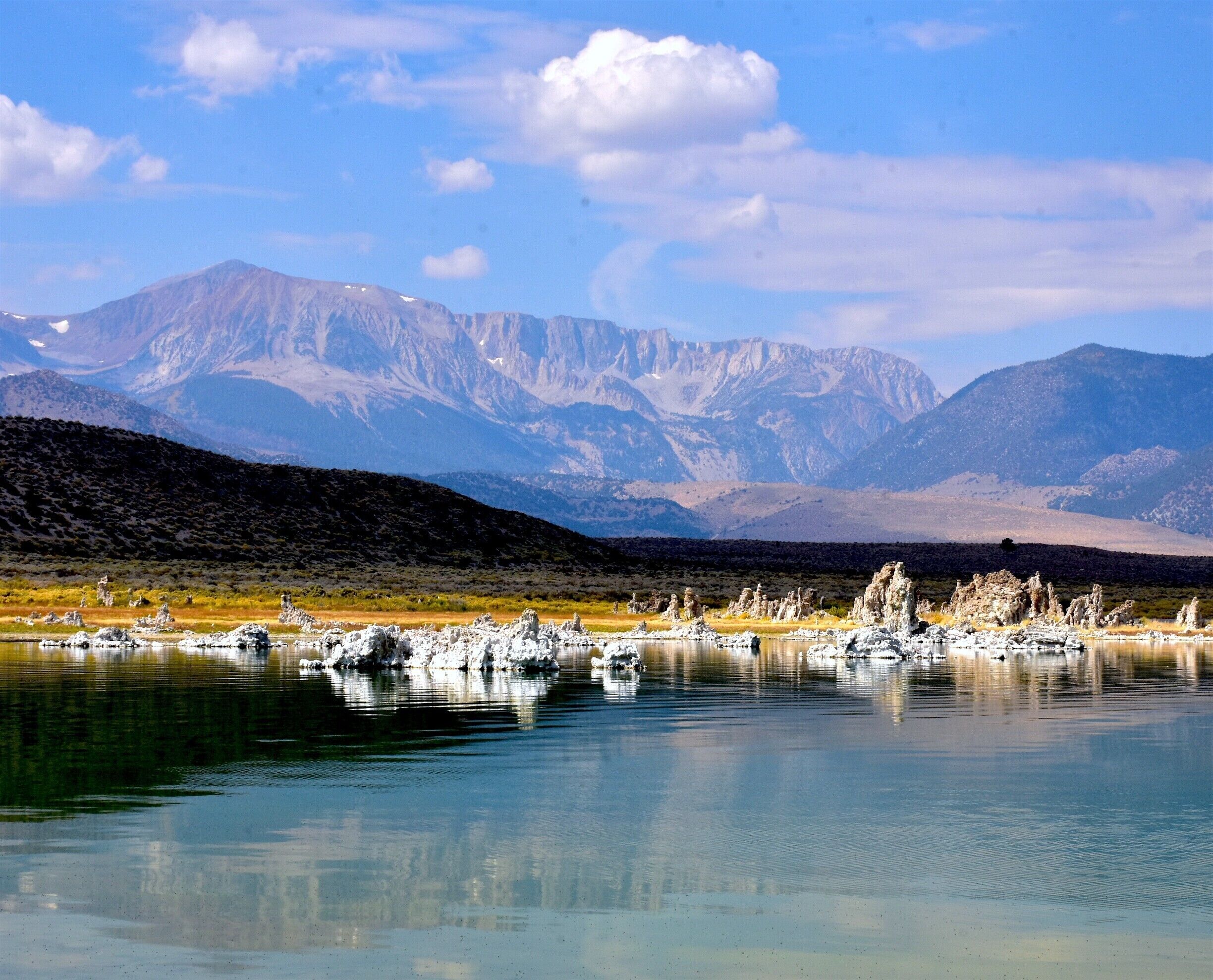 A lake with white rock formations in the foreground and mountains in the background.