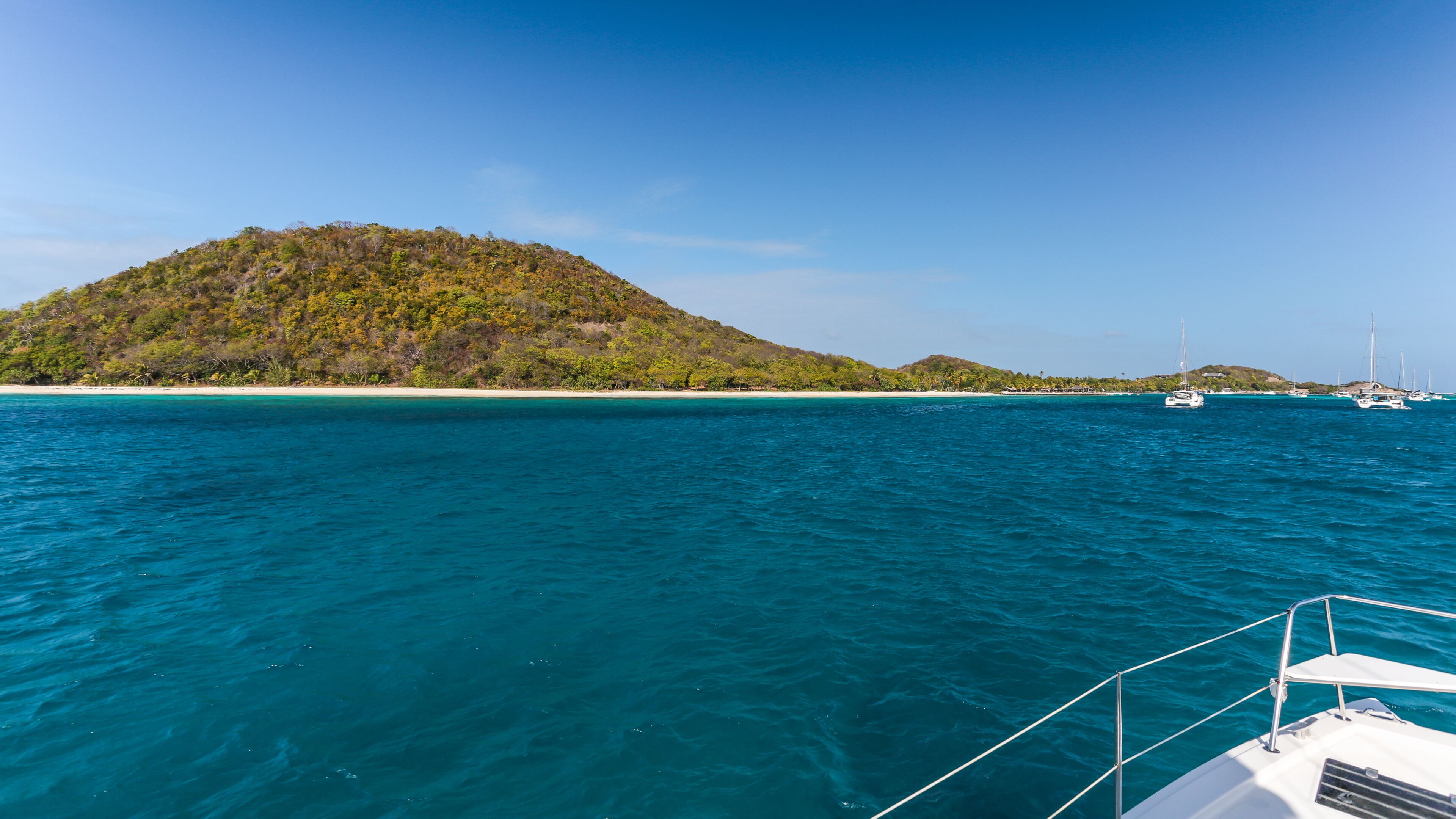A clear blue sea with a boat in the foreground and a small island with dense green vegetation in the background.