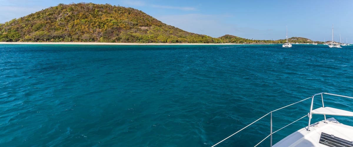 A clear blue sea with a boat in the foreground and a small island with dense green vegetation in the background.