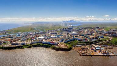 An aerial view of a coastal industrial area with shipping containers, a port, and a distant mountain range.