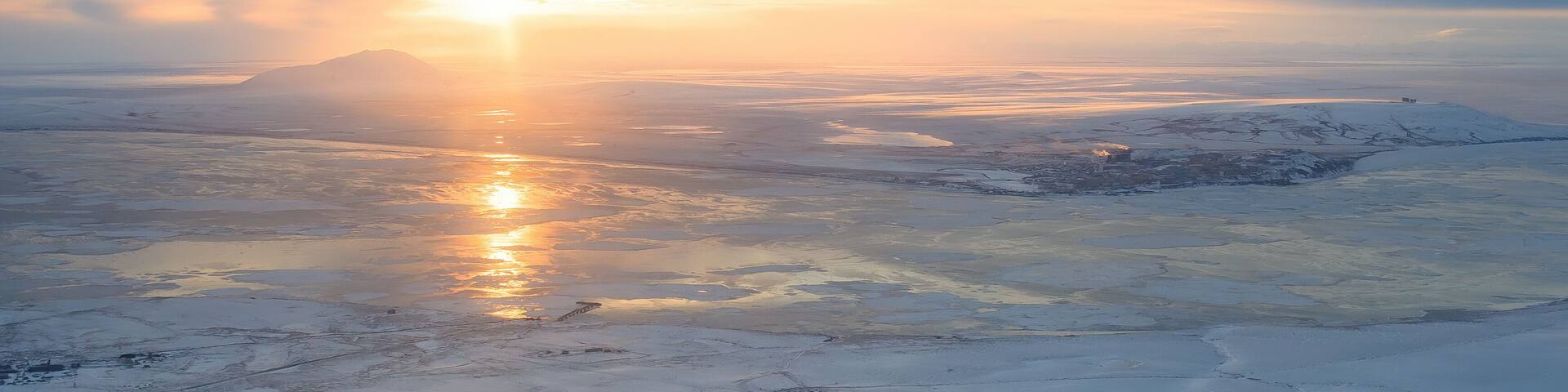Panoramic aerial view of sunset. Arctic landscape. The northern city of Anadyr is located on the banks of the Anadyr estuary, surrounded by snow-covered tundra. Cold autumn in Chukotka Region. Russia.