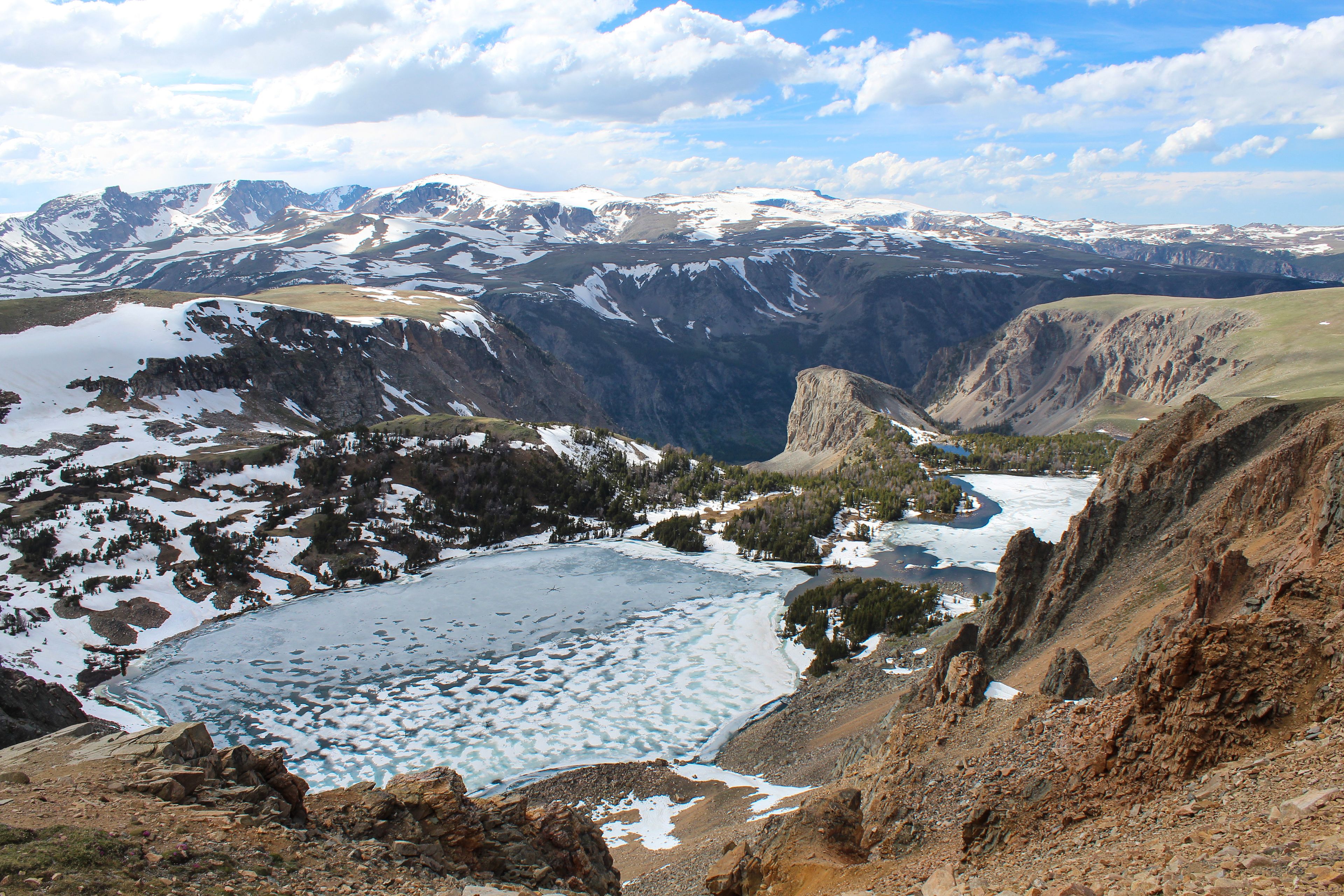 A mountainous landscape with a glacial lake surrounded by rocky terrain and snow-covered peaks.