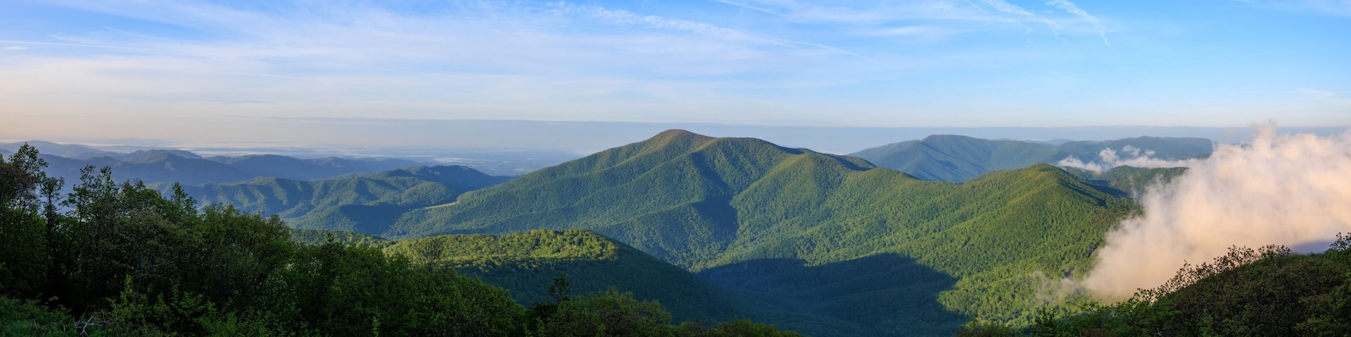 A mountainous landscape with lush green hills and a clear blue sky with contrails.