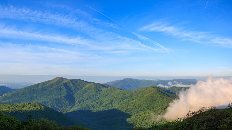 A mountainous landscape with lush green hills and a clear blue sky with contrails.