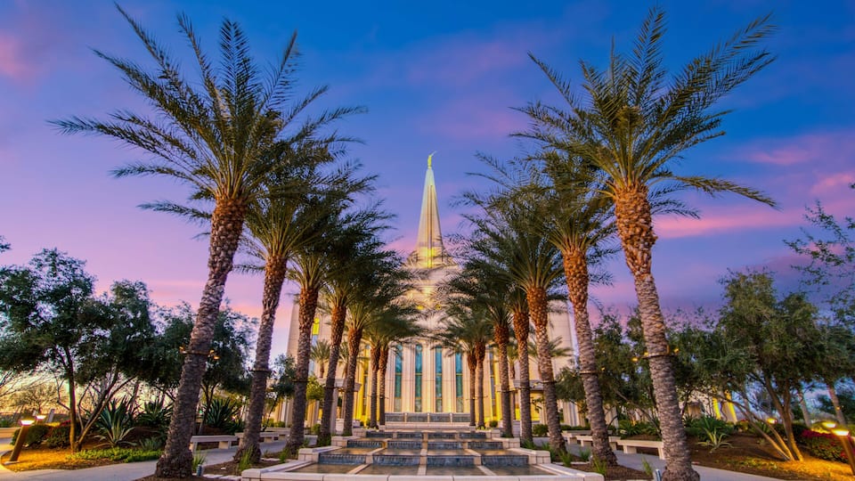 A grand building with a tall spire, surrounded by palm trees and a well-maintained garden.