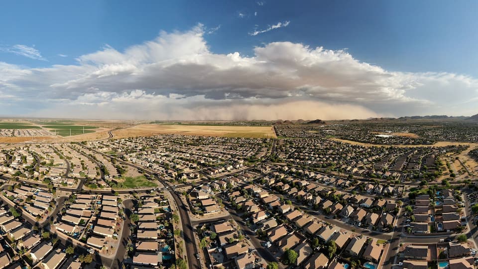 An aerial view of a residential area with houses, roads, and a large cloud formation in the distance.