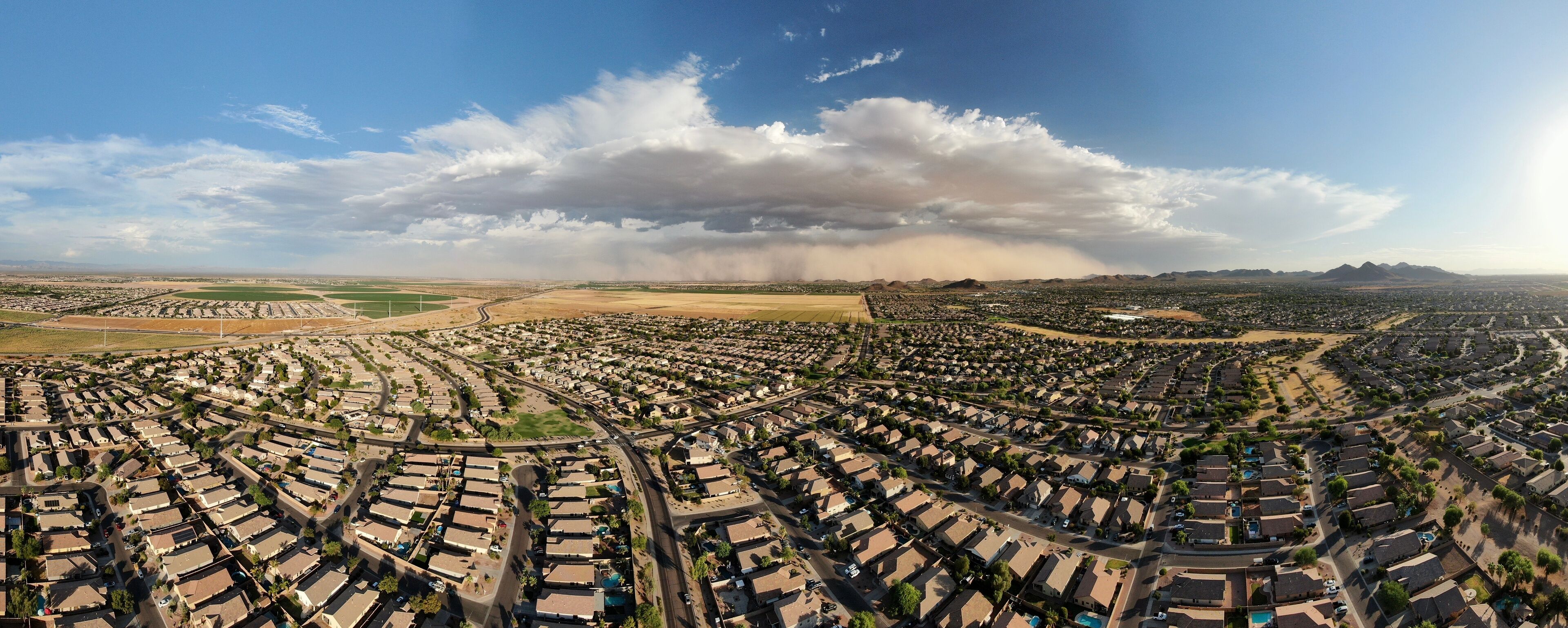 An aerial view of a residential area with houses, roads, and a large cloud formation in the distance.