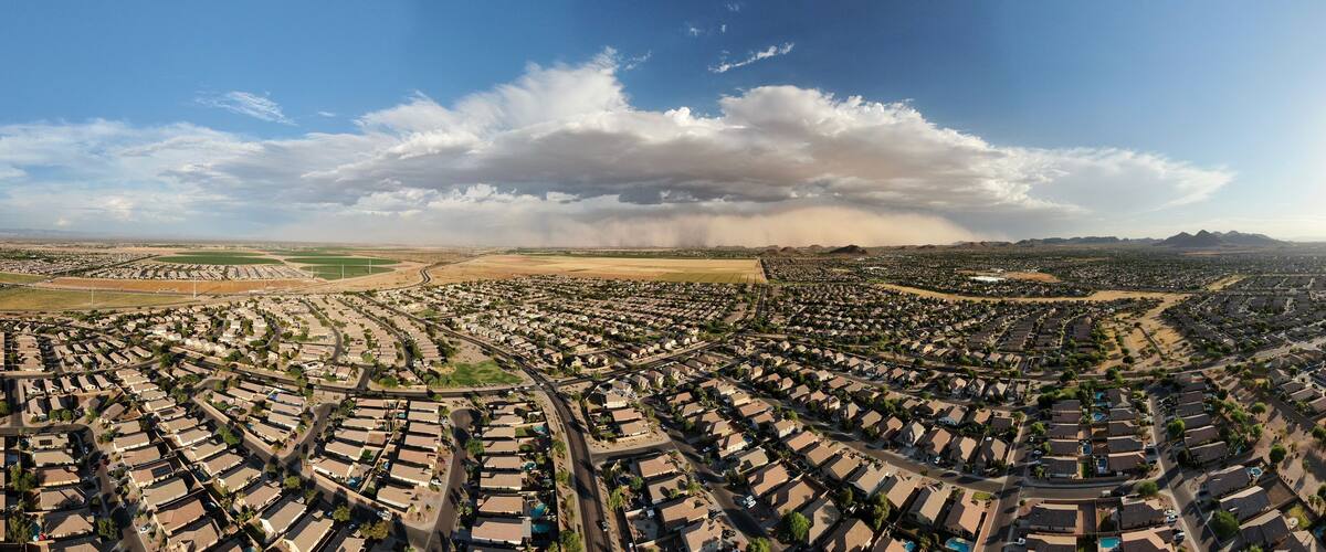 An aerial view of a residential area with houses, roads, and a large cloud formation in the distance.