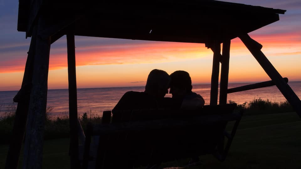 A wooden gazebo overlooking a sunset over the ocean.