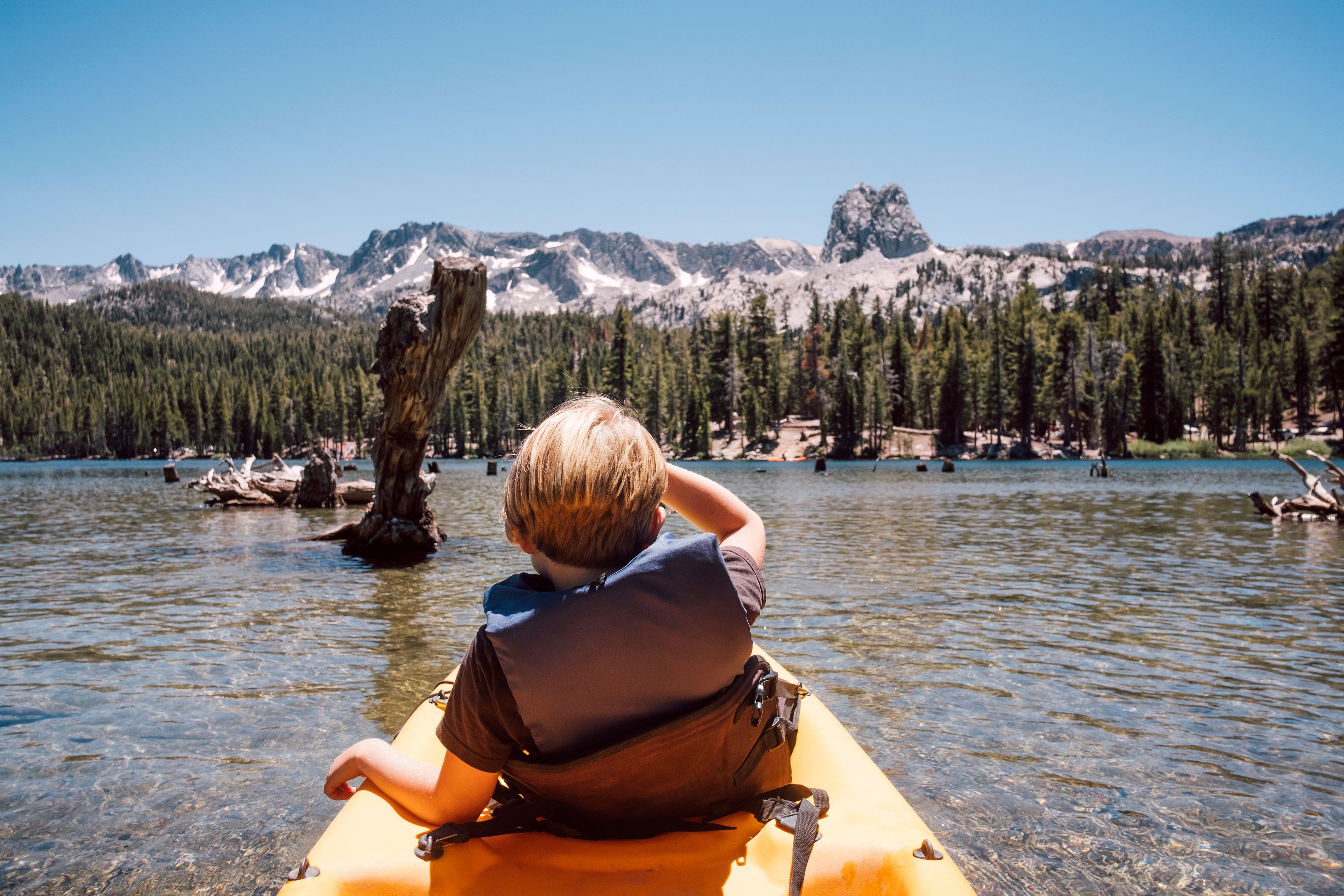 Una persona en un kayak sobre un lago tranquilo, con montañas al fondo.