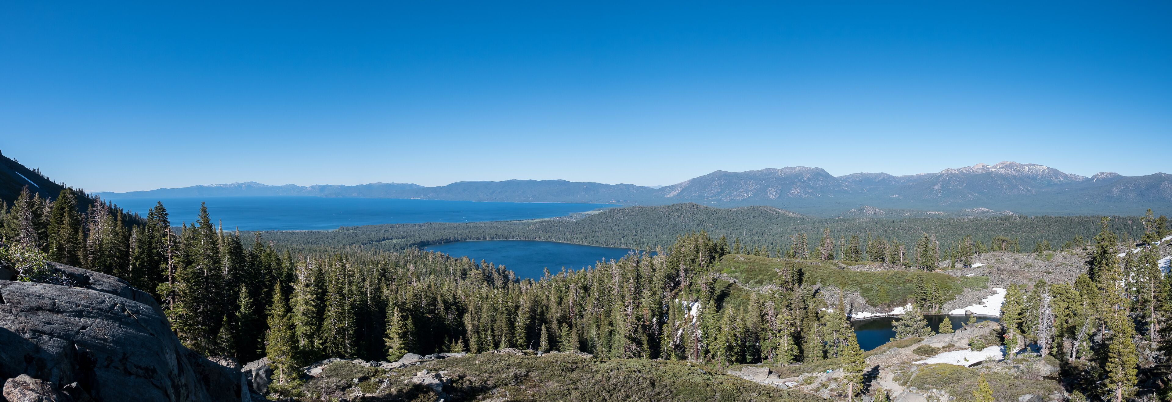 A mountainous landscape with a lake surrounded by dense forests and snow-capped peaks.