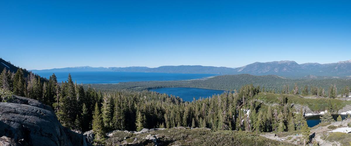 A mountainous landscape with a lake surrounded by dense forests and snow-capped peaks.