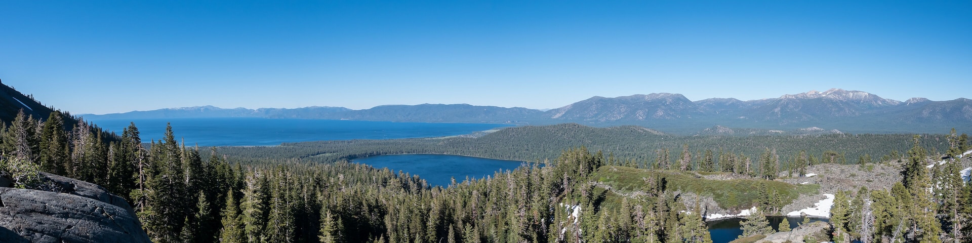 A mountainous landscape with a lake surrounded by dense forests and snow-capped peaks.