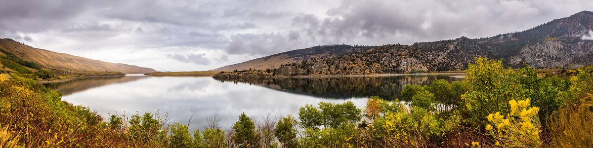 Un lac paisible, entouré de montagnes et bordé d’un feuillage automnal.