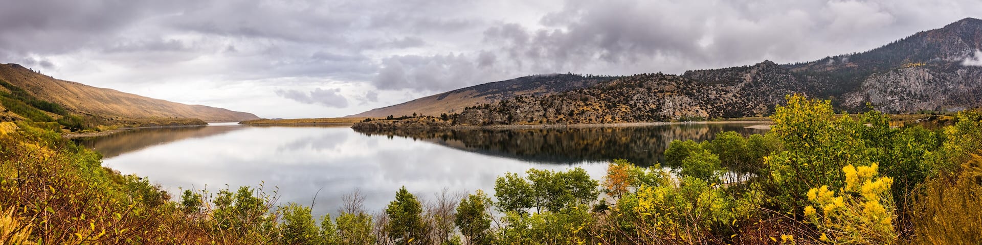 A calm lake surrounded by mountains and autumn foliage.