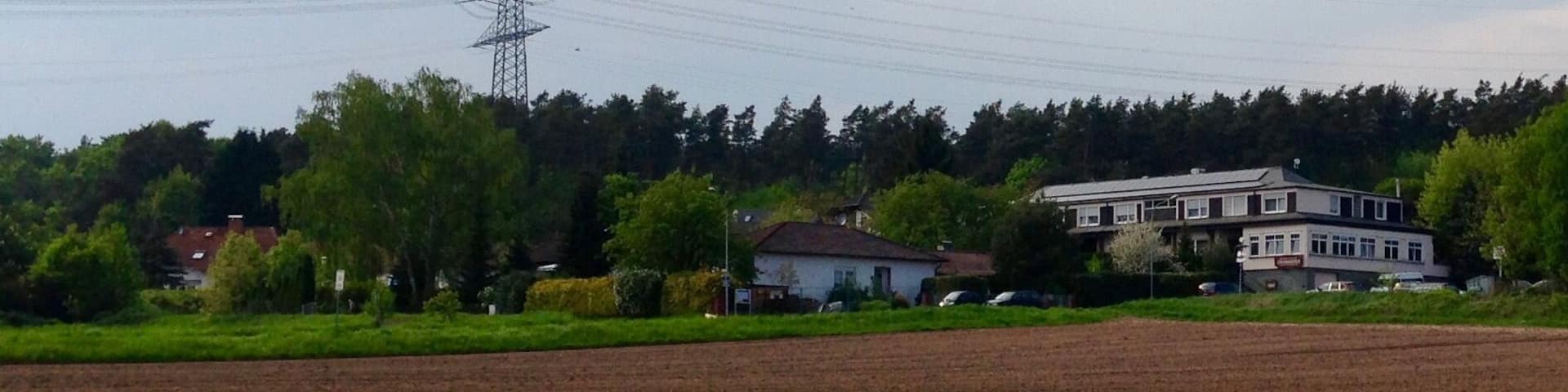 Der Stadtteil Bulau der Stadt Rödermark von einem parallel zu Dreieichbahn verlaufenden Fahrradweg aus fotografiert. Auf der rechten Bildseite ist das ansässige Hotel zu erkennen. Im oberen Bereich des Bildes sind Hochspannungsleitungen zum/vom Umspannwerk Urberach abgebildet.