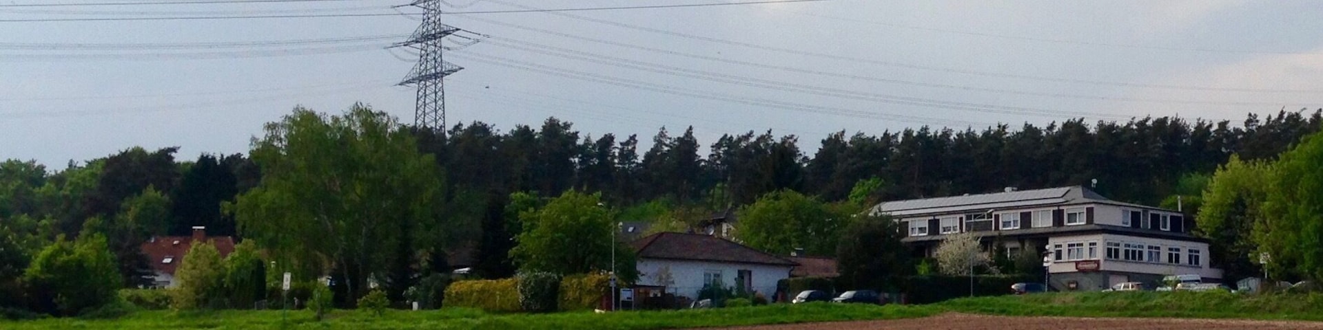Der Stadtteil Bulau der Stadt Rödermark von einem parallel zu Dreieichbahn verlaufenden Fahrradweg aus fotografiert. Auf der rechten Bildseite ist das ansässige Hotel zu erkennen. Im oberen Bereich des Bildes sind Hochspannungsleitungen zum/vom Umspannwerk Urberach abgebildet.