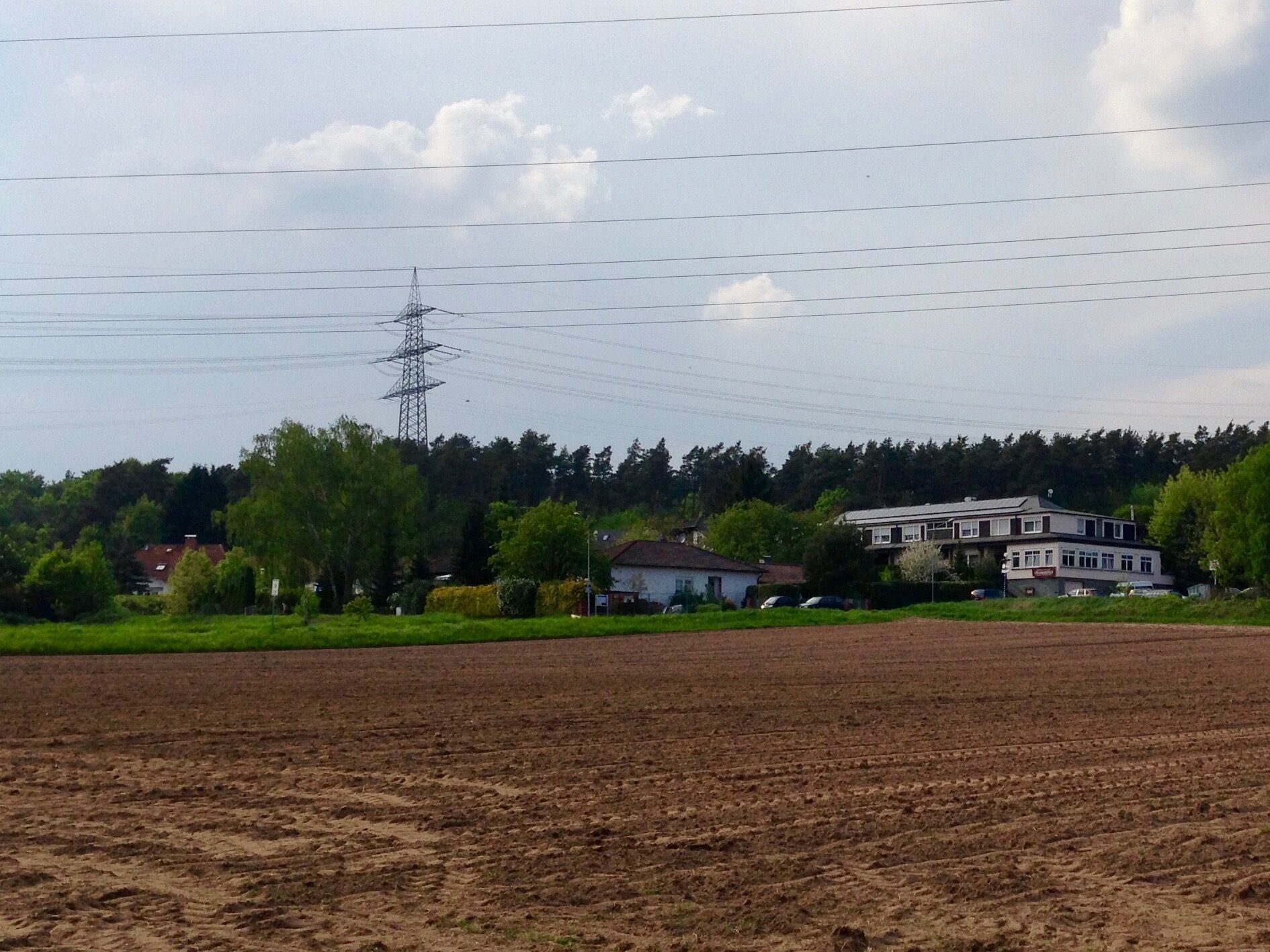 A rural landscape with a large open field, a power line tower, and a two-story house with a white roof.