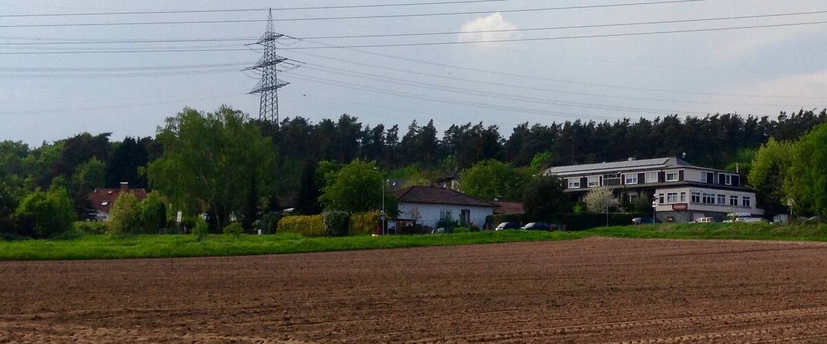 A rural landscape with a large open field, a power line tower, and a two-story house with a white roof.